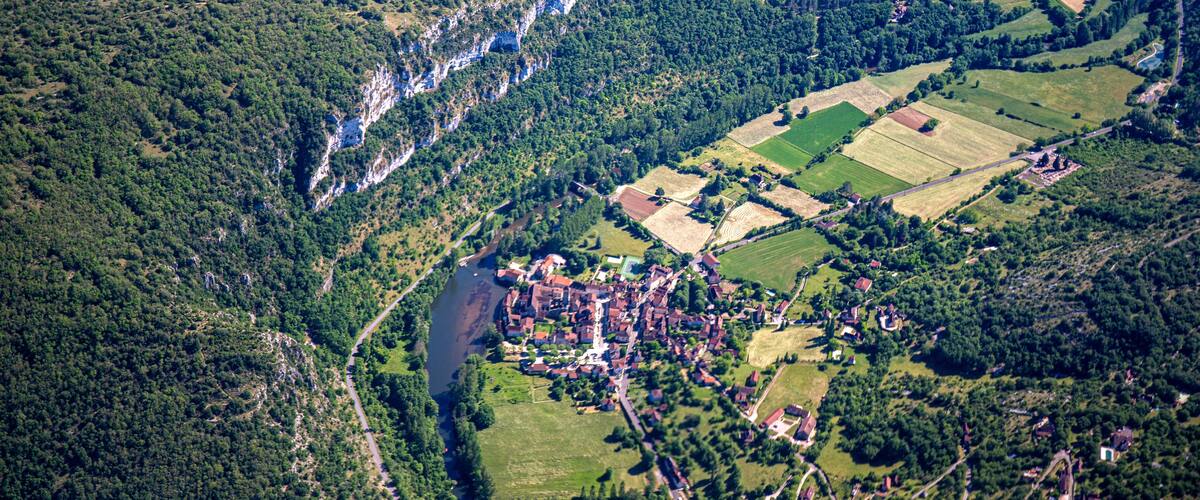 An aerial view of a village surrounded by forested hills and fields.