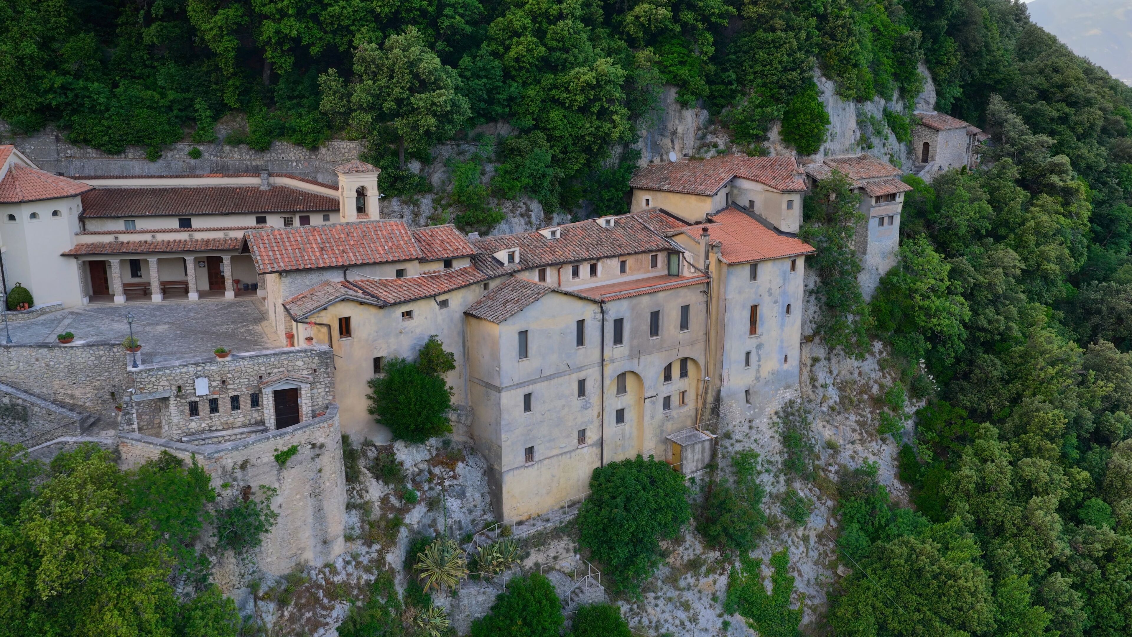 A historic stone building with red-tiled roofs perched on a hillside.