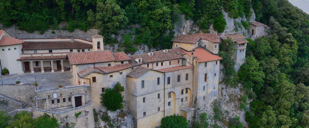 A historic stone building with red-tiled roofs perched on a hillside.