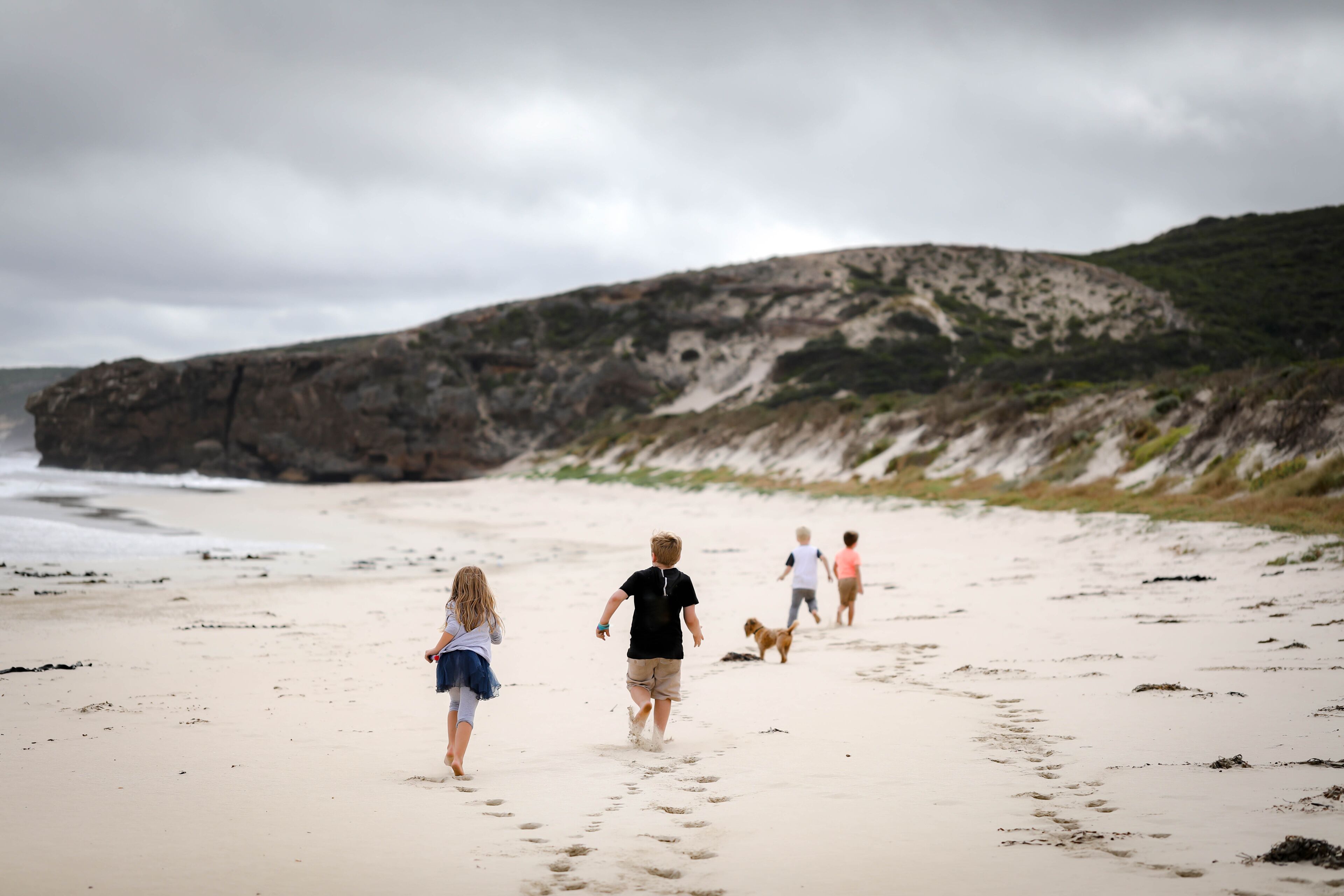 Children running along beach towards large rocky cliff at Portland, Victoria Australia