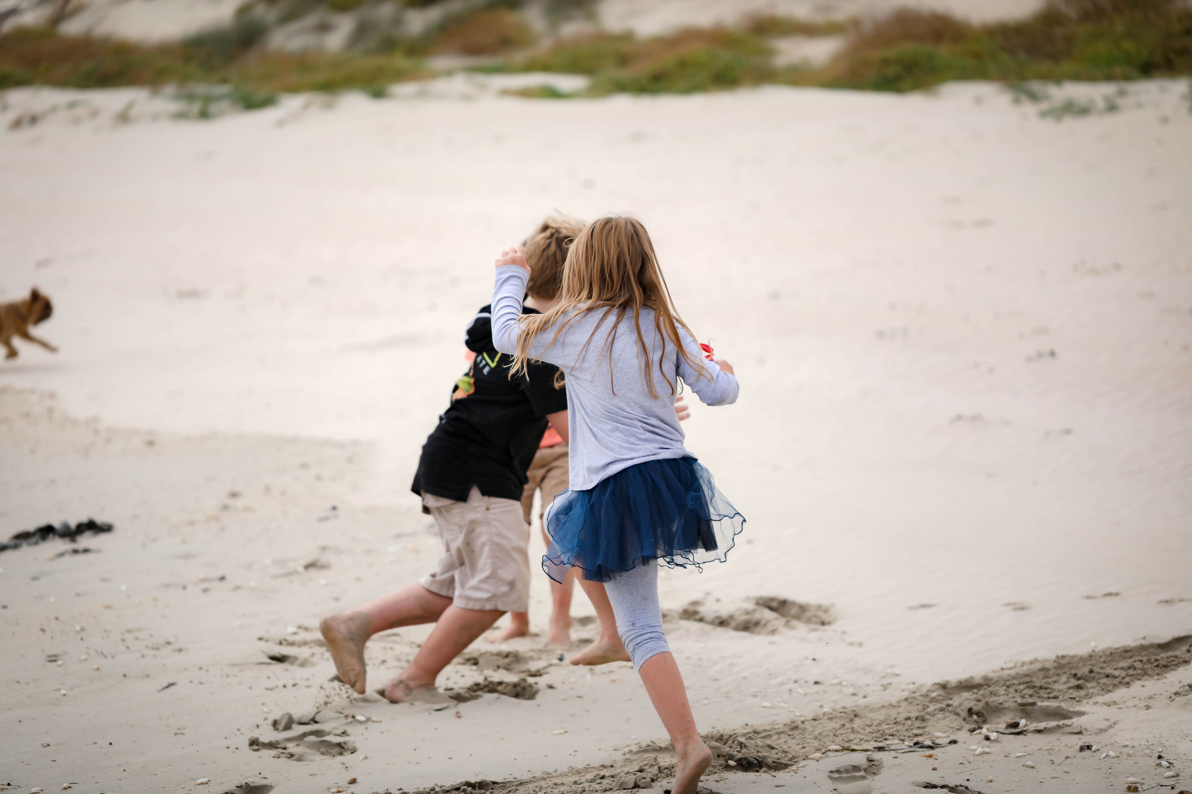 Children playing on a sandy beach with footprints visible.