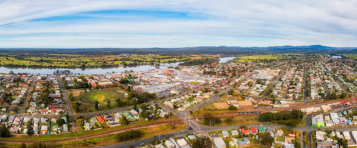 A panoramic view of a town with a river, green fields, and a mountainous backdrop.