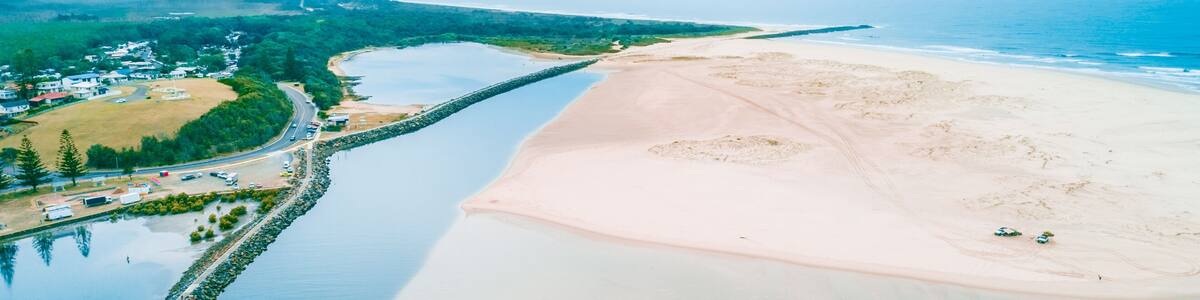 A coastal landscape with a sandy beach, a calm river, and a small settlement with buildings and greenery.