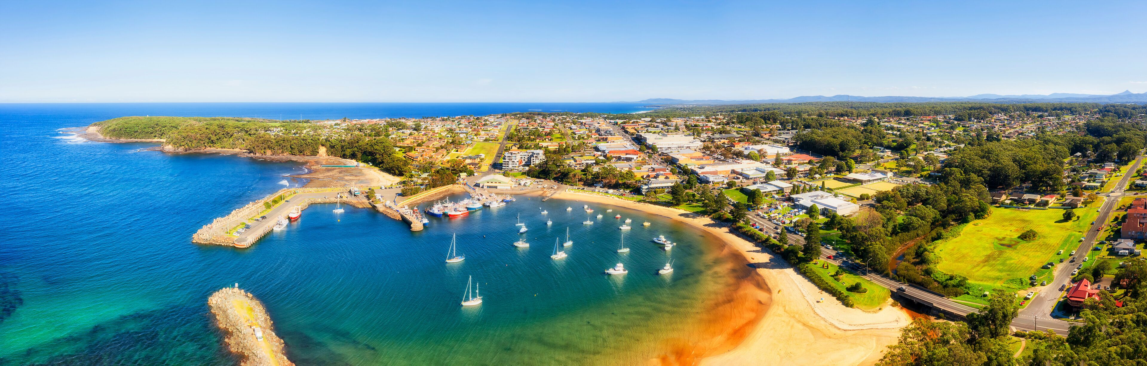 An aerial view of a coastal town with a marina, sandy beaches, and residential areas.