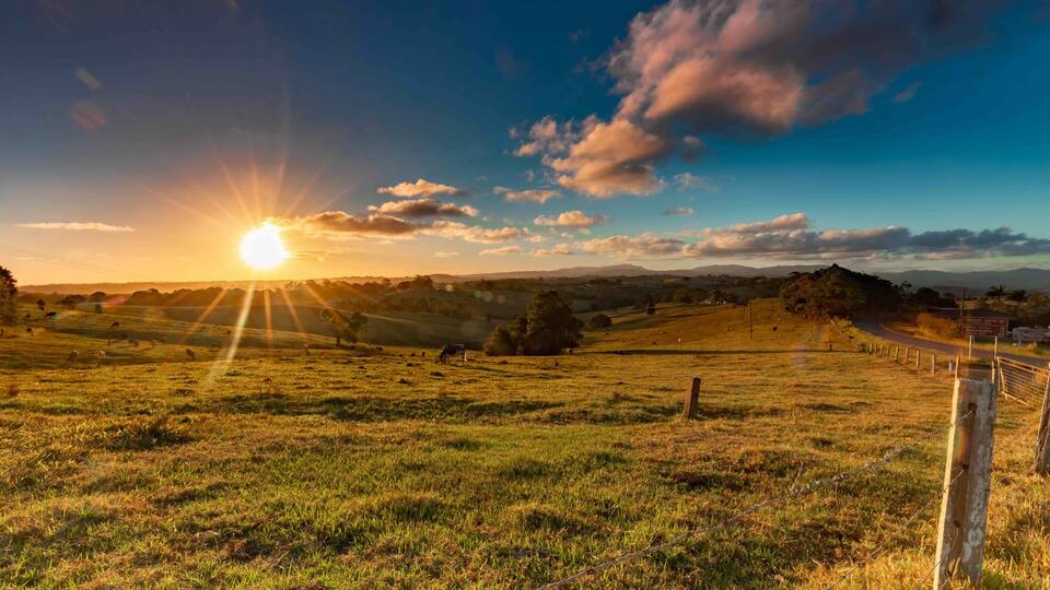 A sunset over a grassy field with a fence and distant hills.