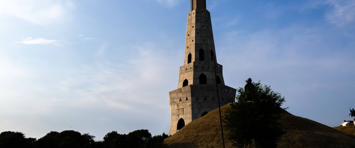 A tall tower with a dome and a cross on top, surrounded by trees and a clear sky.