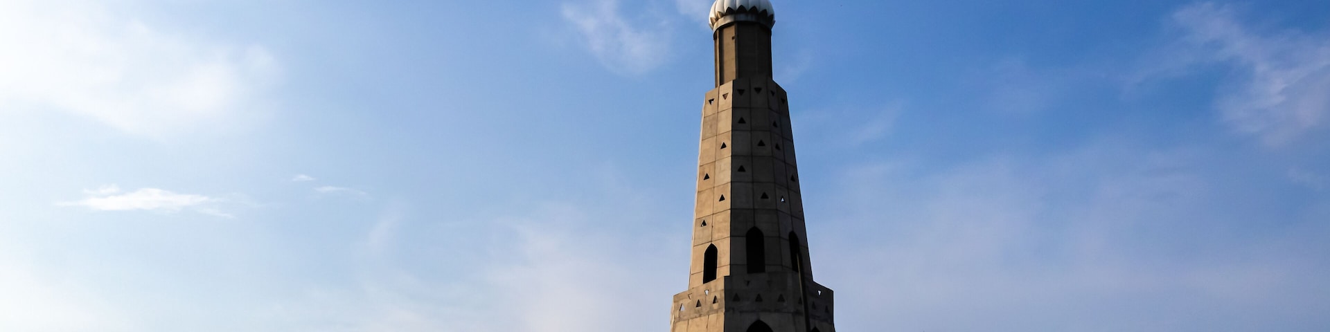 A tall tower with a dome and a cross on top, surrounded by trees and a clear sky.
