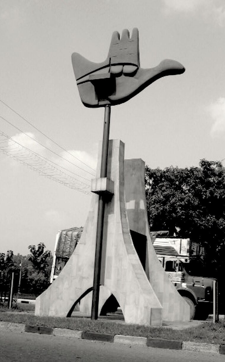 A large hand sculpture on a pole, surrounded by a concrete structure with arches.