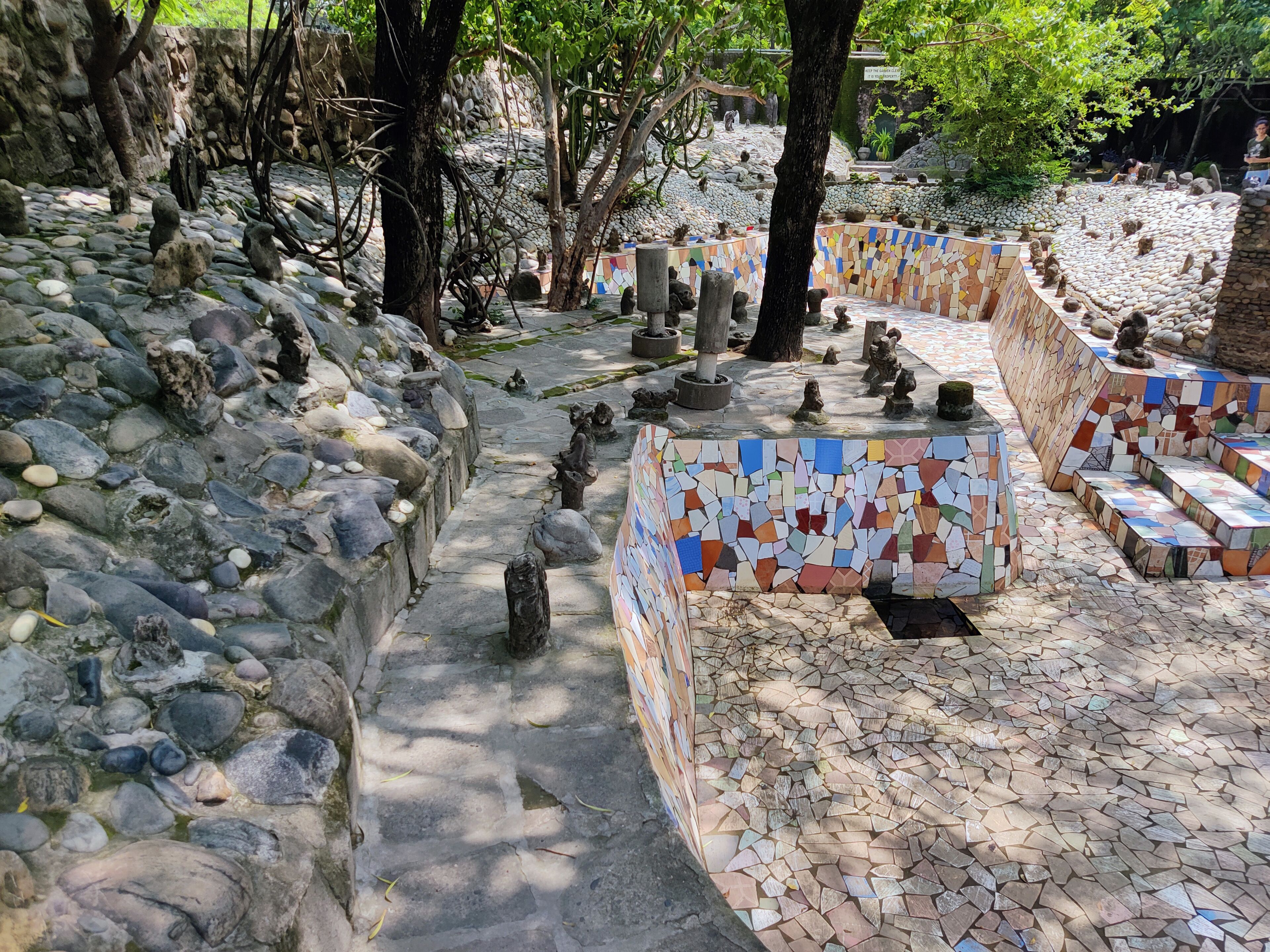 Un sendero de piedra con estatuas y paredes cubiertas de mosaicos en un jardín.