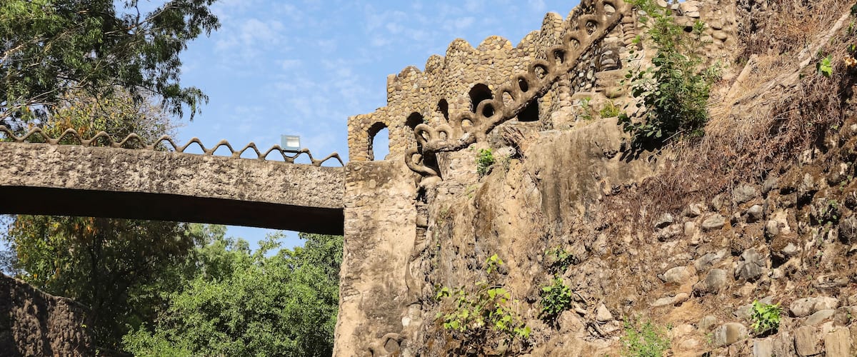A stone bridge with a unique serpentine design, a stone wall with circular cutouts, and lush green trees in the background.