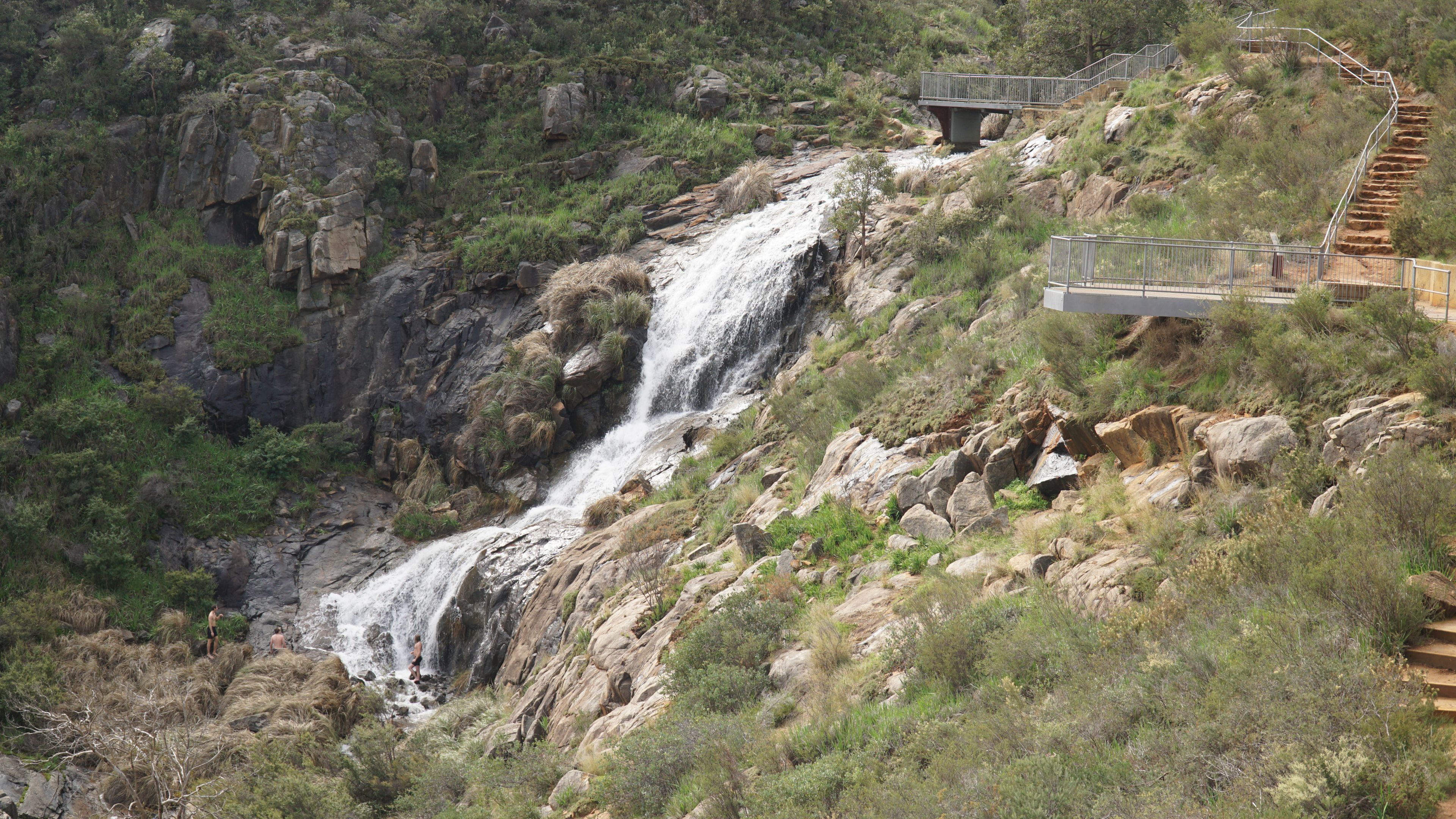 A waterfall cascading down a rocky hillside with a bridge and stairs leading up to it.