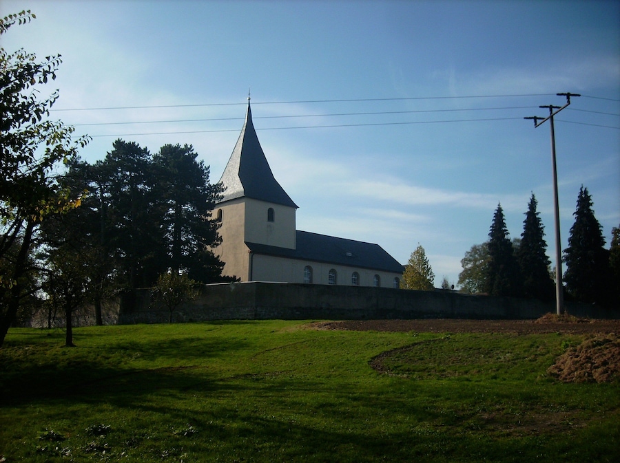A church with a tall steeple and a stone wall in front.