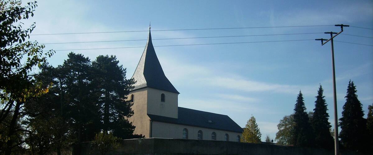 A church with a tall steeple and a stone wall in front.