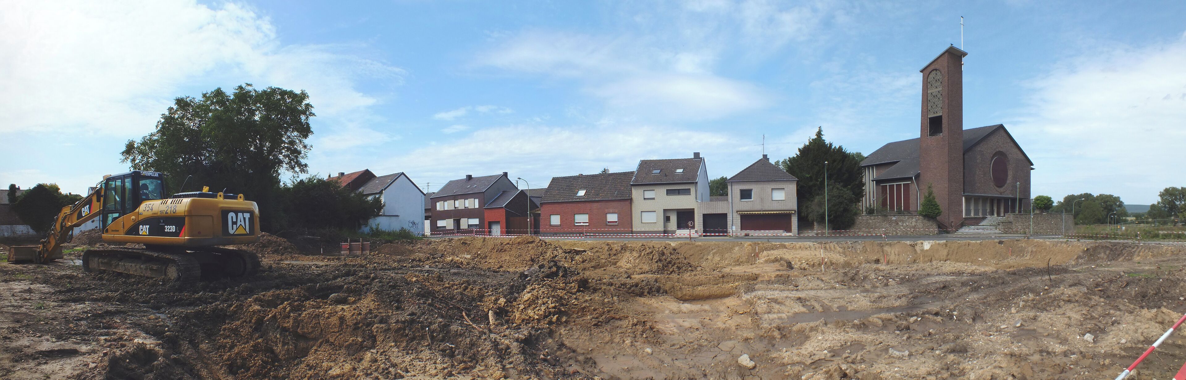 A construction site with a yellow excavator and a church with a tall tower.