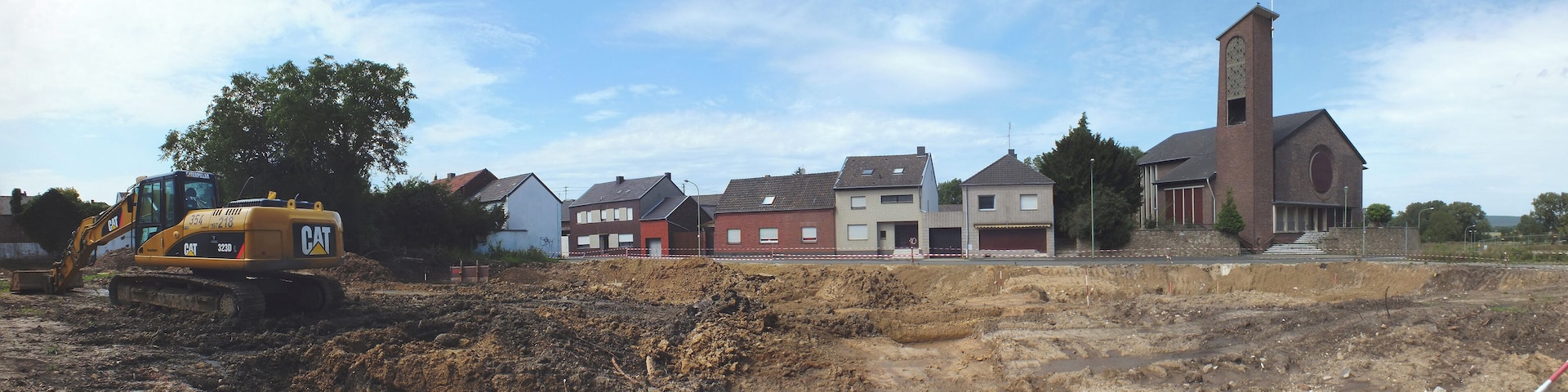 A construction site with a yellow excavator and a church with a tall tower.