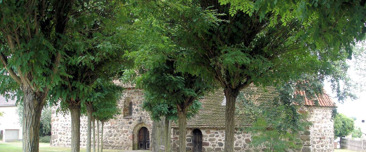 A stone building with a tiled roof, surrounded by trees and a paved pathway.