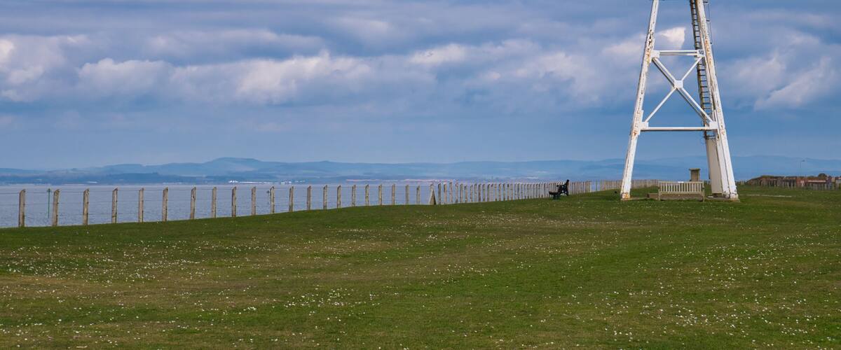 A lighthouse on a grassy hill with a cloudy sky.