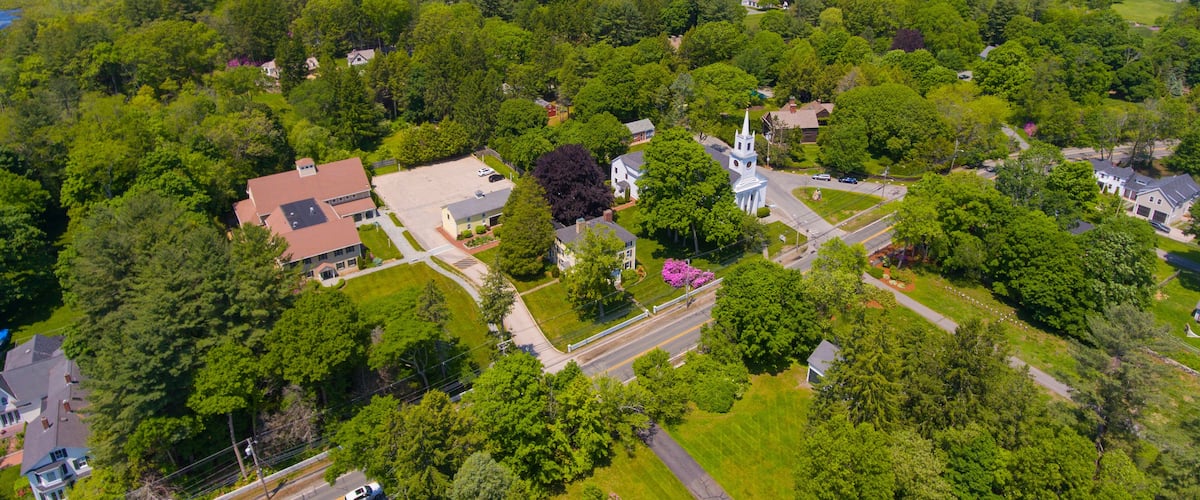 A lush green landscape with a white church, residential houses, and a clear road.