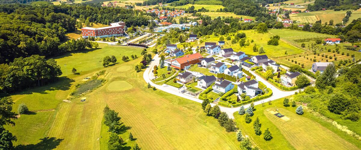 An aerial view of a residential area with houses, green fields, and a large building.