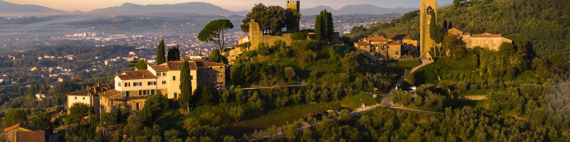 A hillside town with historic stone buildings, a prominent tower, and a view of the distant cityscape.