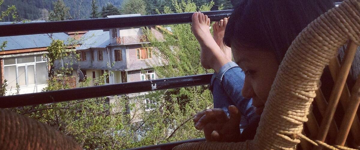 A person sitting on a woven chair overlooking a mountainous landscape with houses and trees.