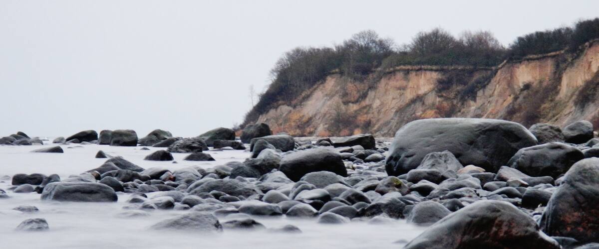 A rocky shoreline with large boulders and a cliff in the background.