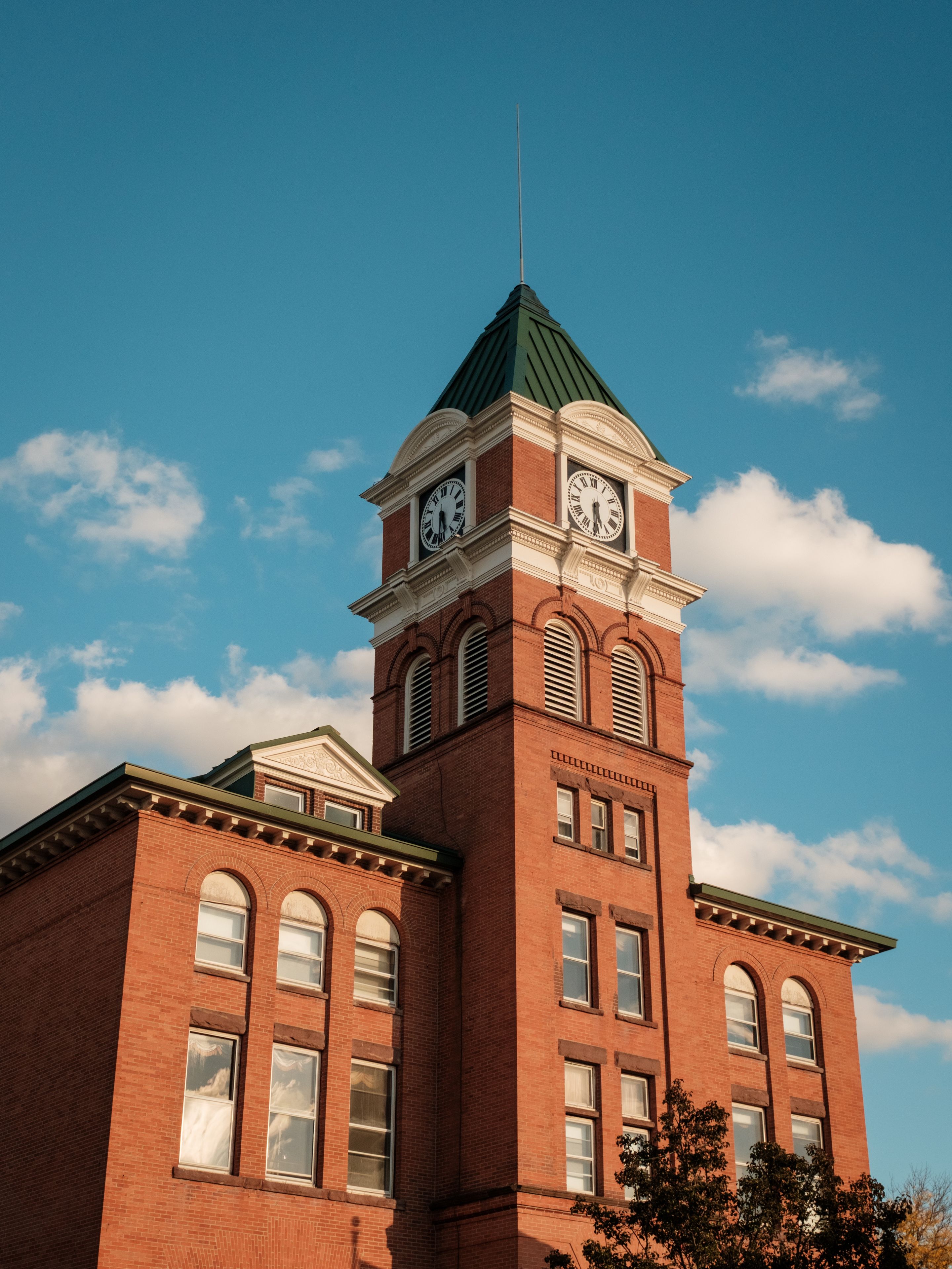 A brick building with a clock tower, arched windows, and a green roof.