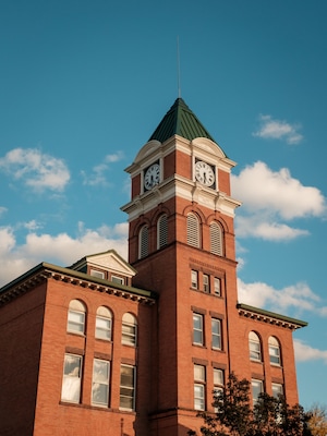 A brick building with a clock tower, arched windows, and a green roof.