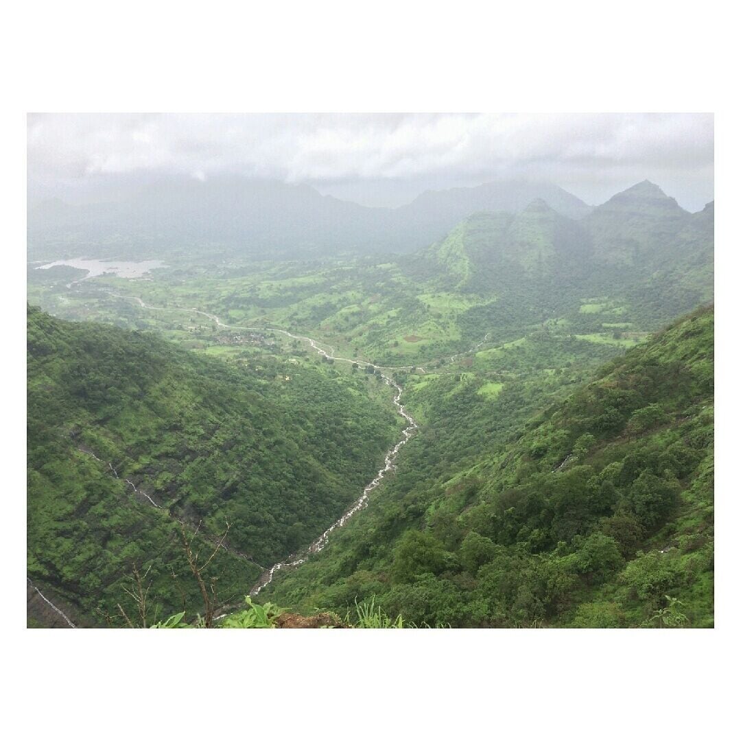 A lush green valley with a winding river and distant mountains under a cloudy sky.