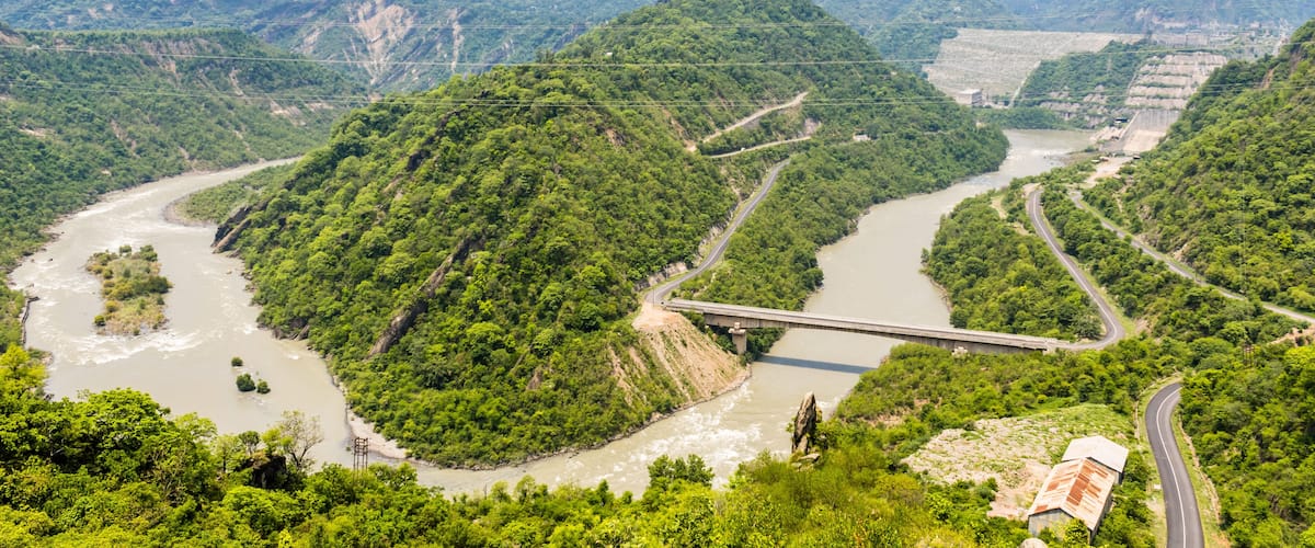 A river winding through lush green hills with a bridge spanning across it.