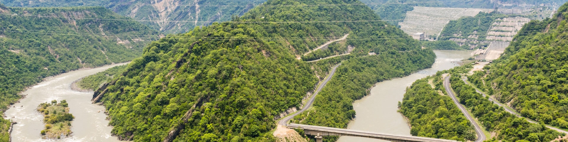A river winding through lush green hills with a bridge spanning across it.