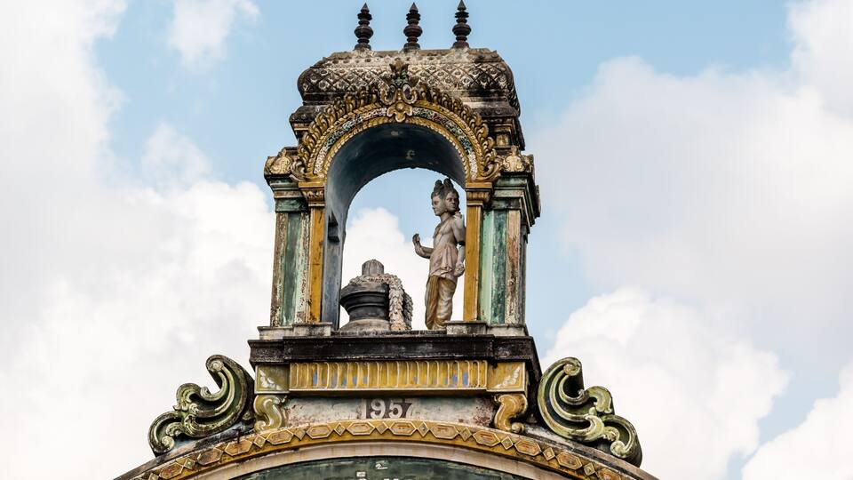 A detailed stone archway with inscriptions and statues, featuring intricate carvings and a clear sky in the background.
