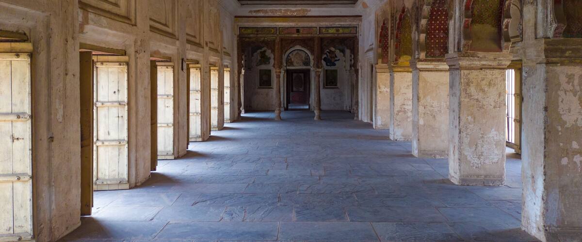 A corridor with stone floors and wooden doors, leading to a central archway.
