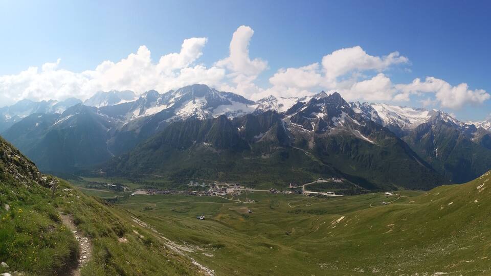 A mountainous landscape with snow-capped peaks, a valley with scattered buildings, and a clear blue sky.