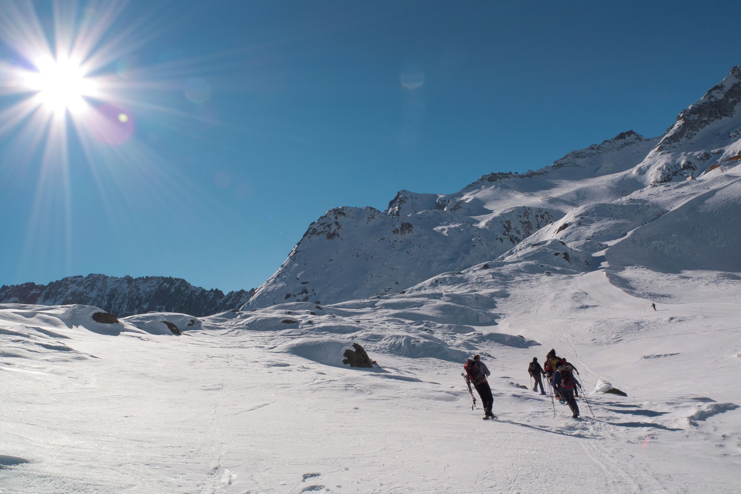 A snowy mountain landscape with skiers and a bright sun in the sky.