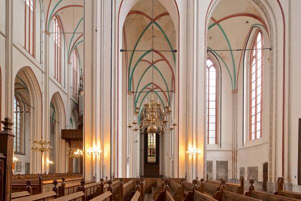 A church interior with high vaulted ceilings, stained glass windows, and wooden pews.