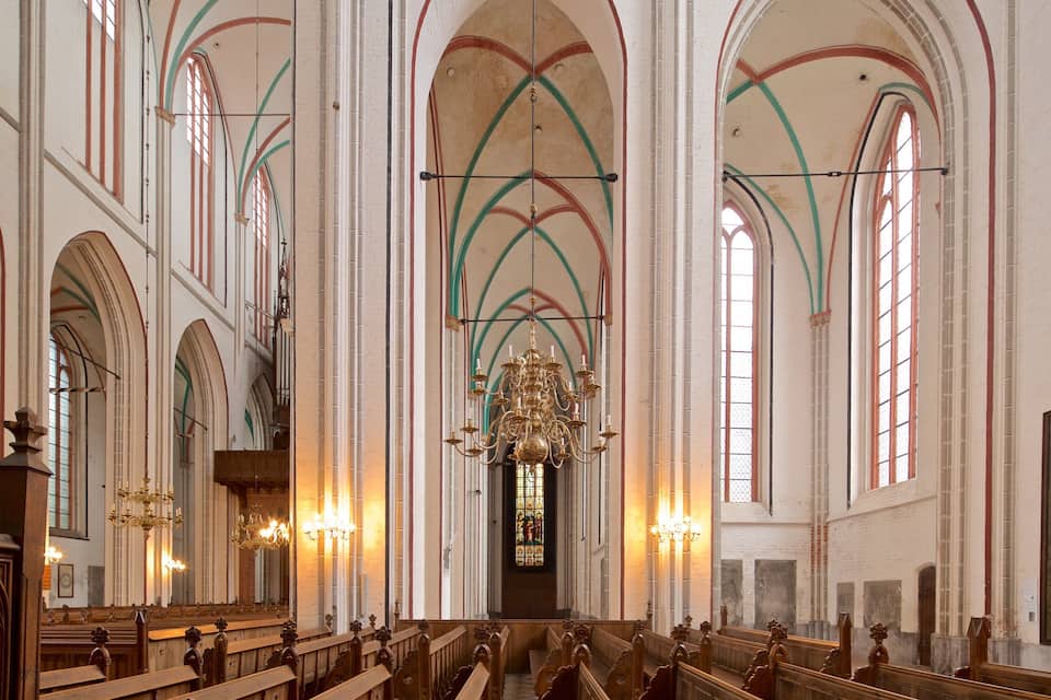 Interior de una iglesia con techos abovedados altos, vidrieras de colores y bancos de madera.