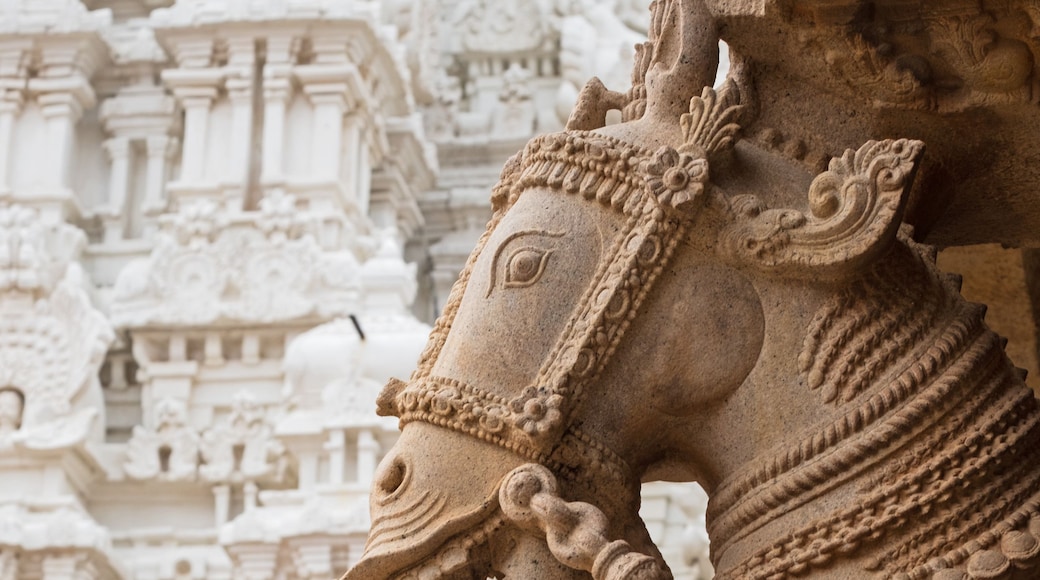 A detailed stone sculpture of a horse with ornate carvings and a rider, set against a temple backdrop.