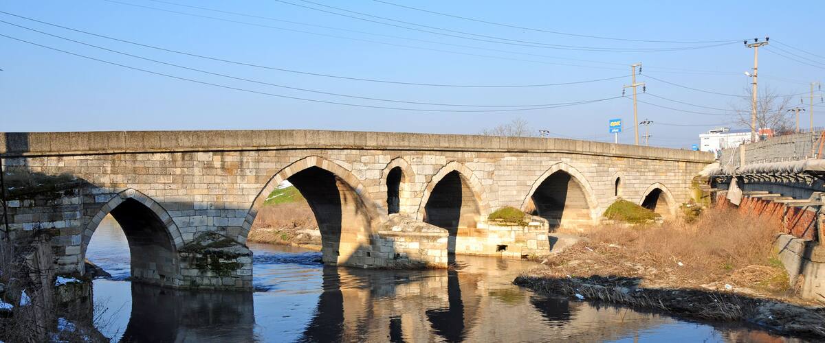 A stone bridge with multiple arches over a calm river.