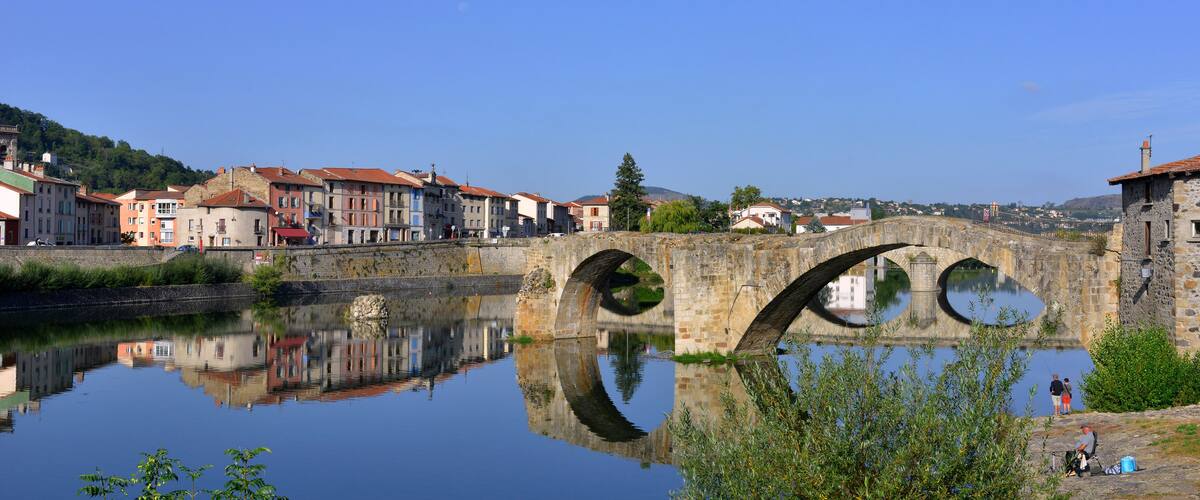 A stone bridge over a calm river, reflecting buildings and trees.