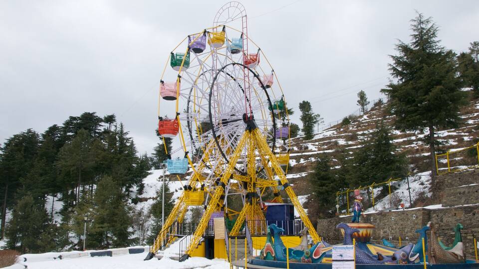A large yellow Ferris wheel with colorful gondolas, surrounded by snow-covered trees and a stone wall.