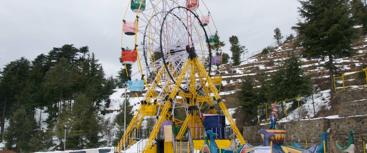 A large yellow Ferris wheel with colorful gondolas, surrounded by snow-covered trees and a stone wall.