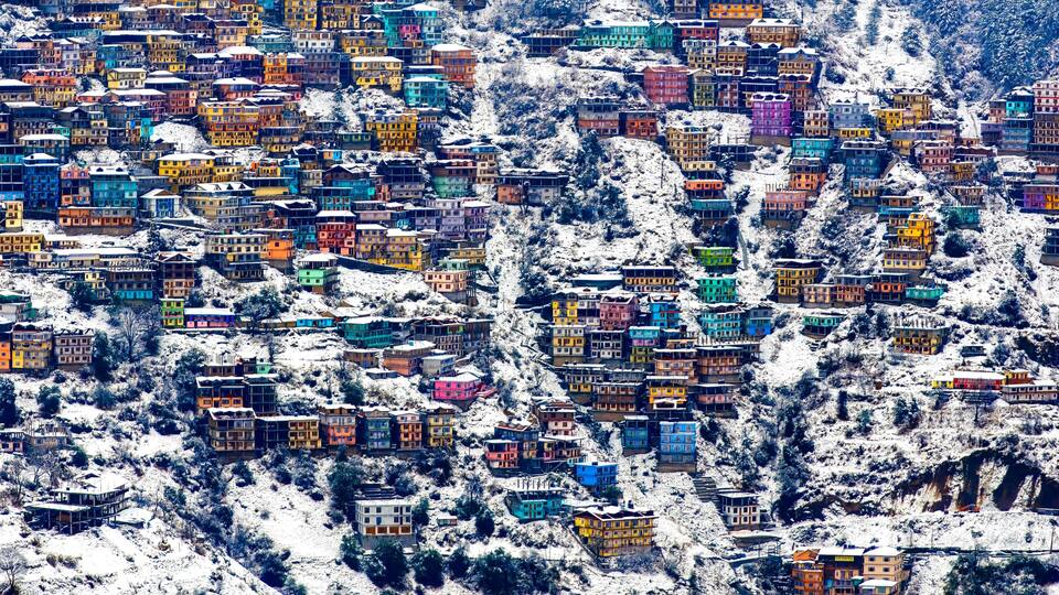 A densely packed hillside village with colorful buildings covered in snow.