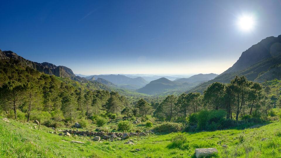 A mountainous landscape with a clear sky and a visible sun.