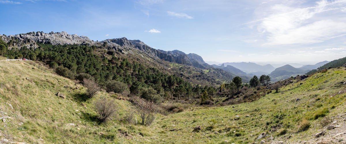 A mountainous landscape with a winding road, dense forests, and rocky terrain.