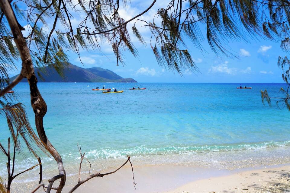 Ein Strand mit klarem türkisblauem Wasser, einer sandigen Küste und mehreren kleinen Booten in der Ferne.