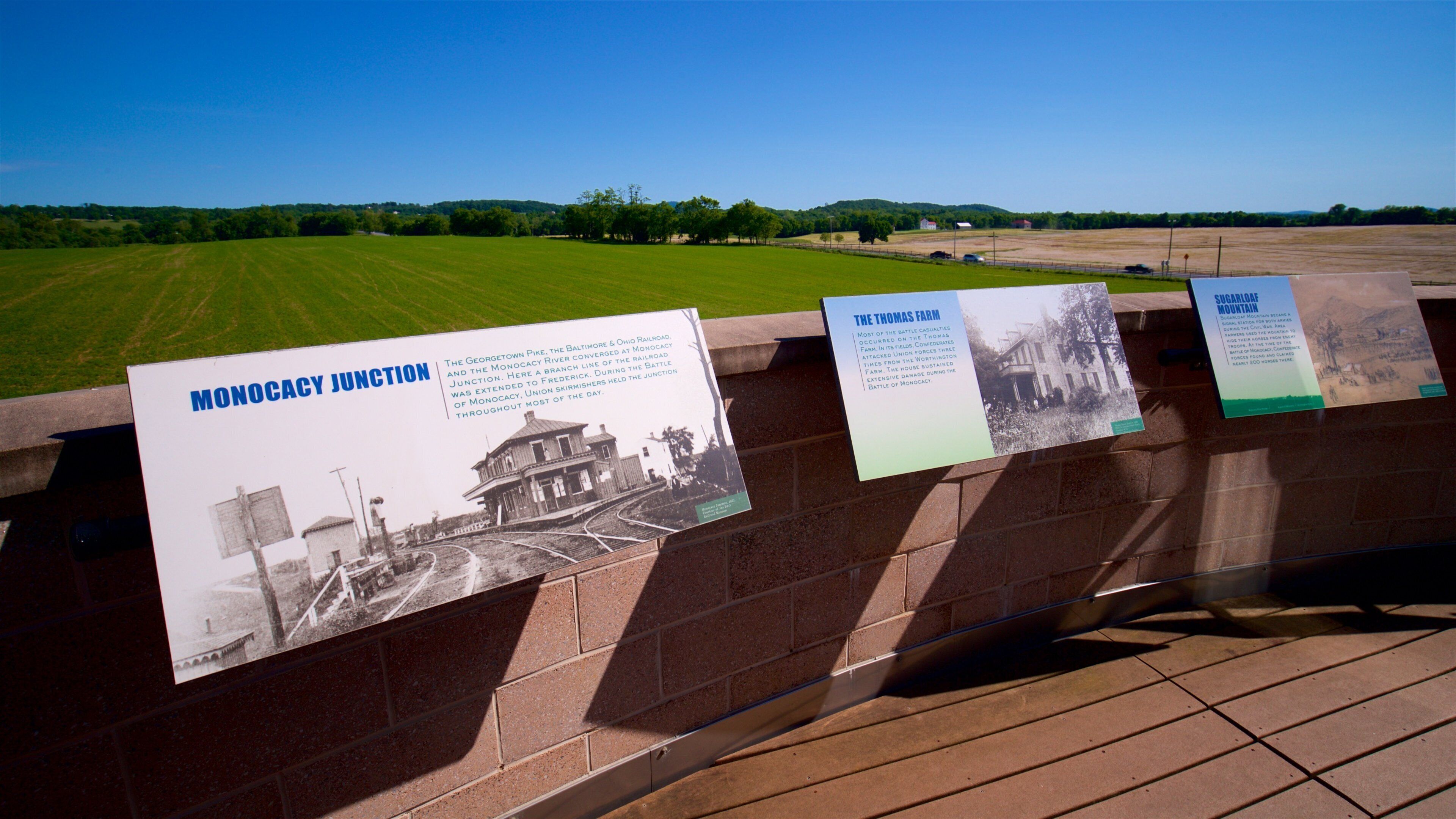 Historical markers on a bridge with a view of a green field and distant hills.