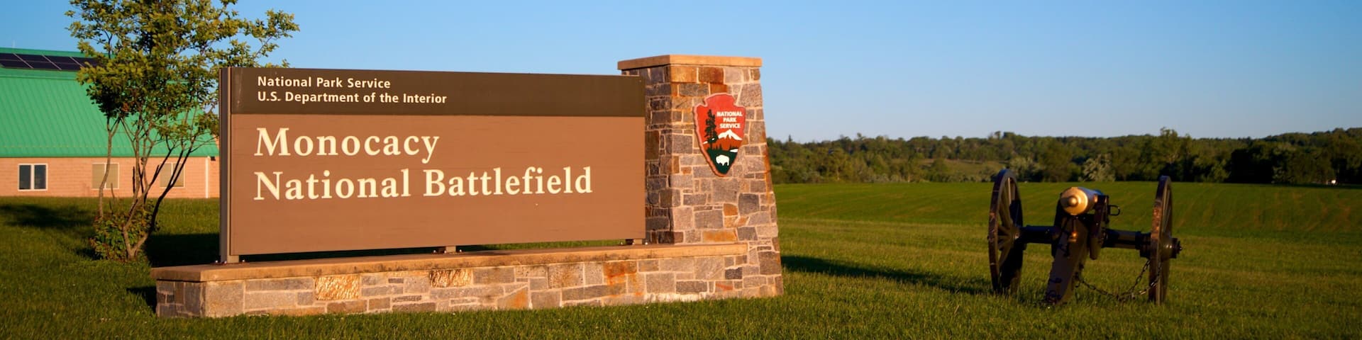 A sign for Monocacy National Battlefield with a stone base and a green building in the background.