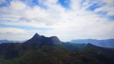 A mountainous landscape with a prominent peak and lush green valleys under a partly cloudy sky.