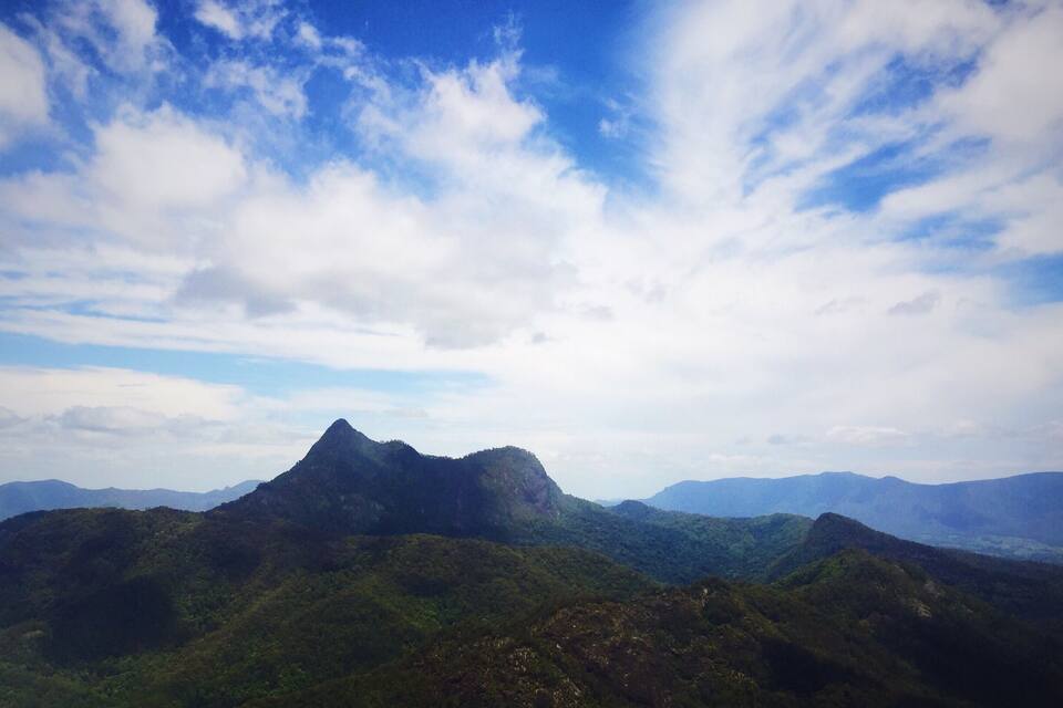 A mountainous landscape with a prominent peak and lush green valleys under a partly cloudy sky.